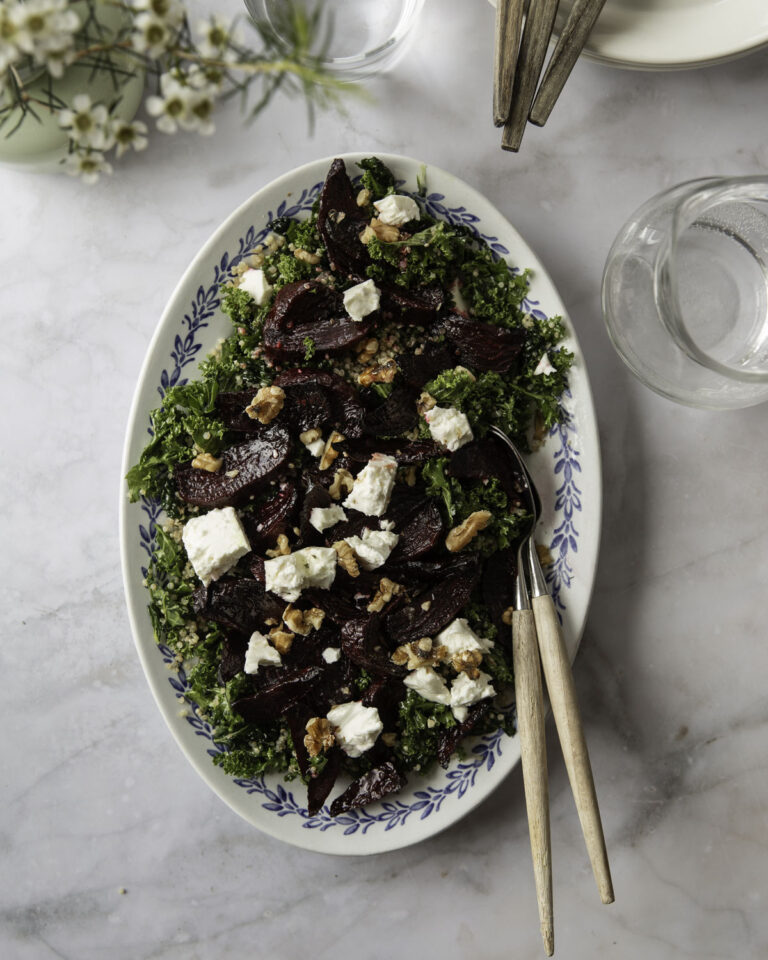 Punajuuri-fetasalaatti on klassikko. Kuvassa salaatti on laakealla vaalealla vadilla, jonka reunoilla on sinistä kuviota. Salaatin pohjana on lehtikaalia ja päällä on saksanpähkinöitä. Kuvan yläreunassa on astioita ja kukkia.