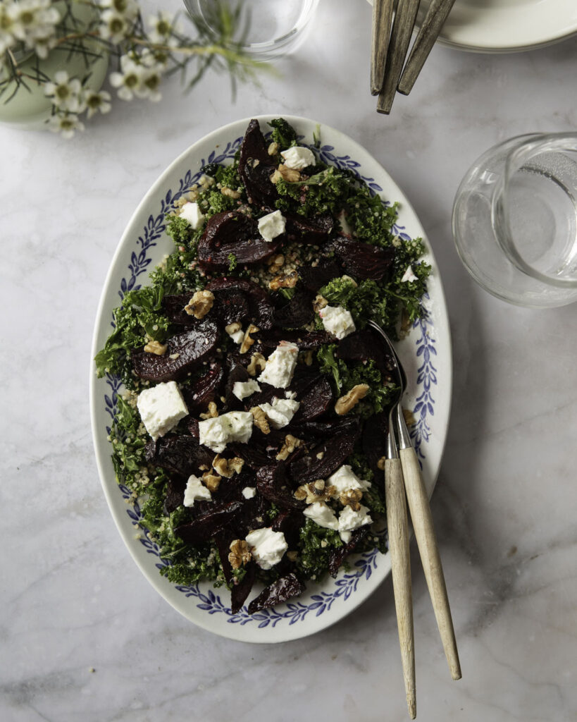 Punajuuri-fetasalaatti on klassikko. Kuvassa salaatti on laakealla vaalealla vadilla, jonka reunoilla on sinistä kuviota. Salaatin pohjana on lehtikaalia ja päällä on saksanpähkinöitä. Kuvan yläreunassa on astioita ja kukkia.