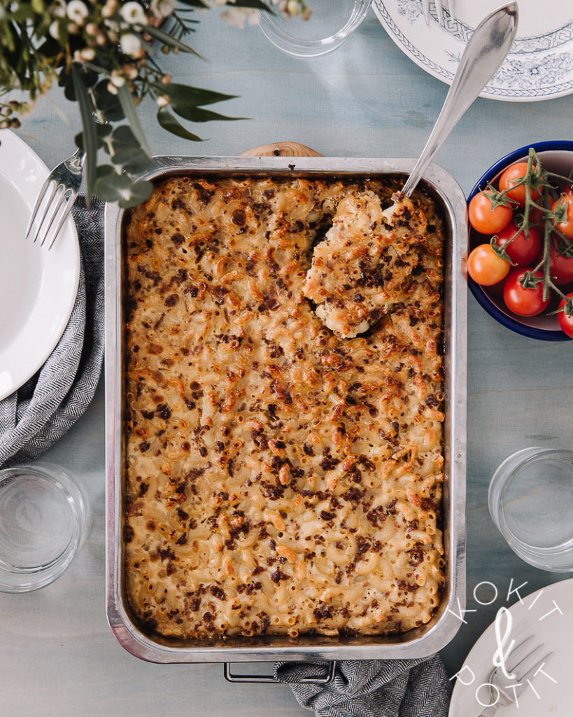 Soijarouhe-makaronilaatikko on helppo arkiruoka. Kuvassa makaronilaatikon ympärillä on lautasia, laseja ja kirsikkatomaatteja. Vasemmassa yläkulmassa on kukkia. Kuva alkusta on vaaleansininen.