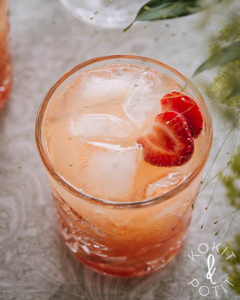 Koristeellinen lasi, jossa on oranssia aperol spritz -juomaa ja jäitä. Koristeena mansikoita.