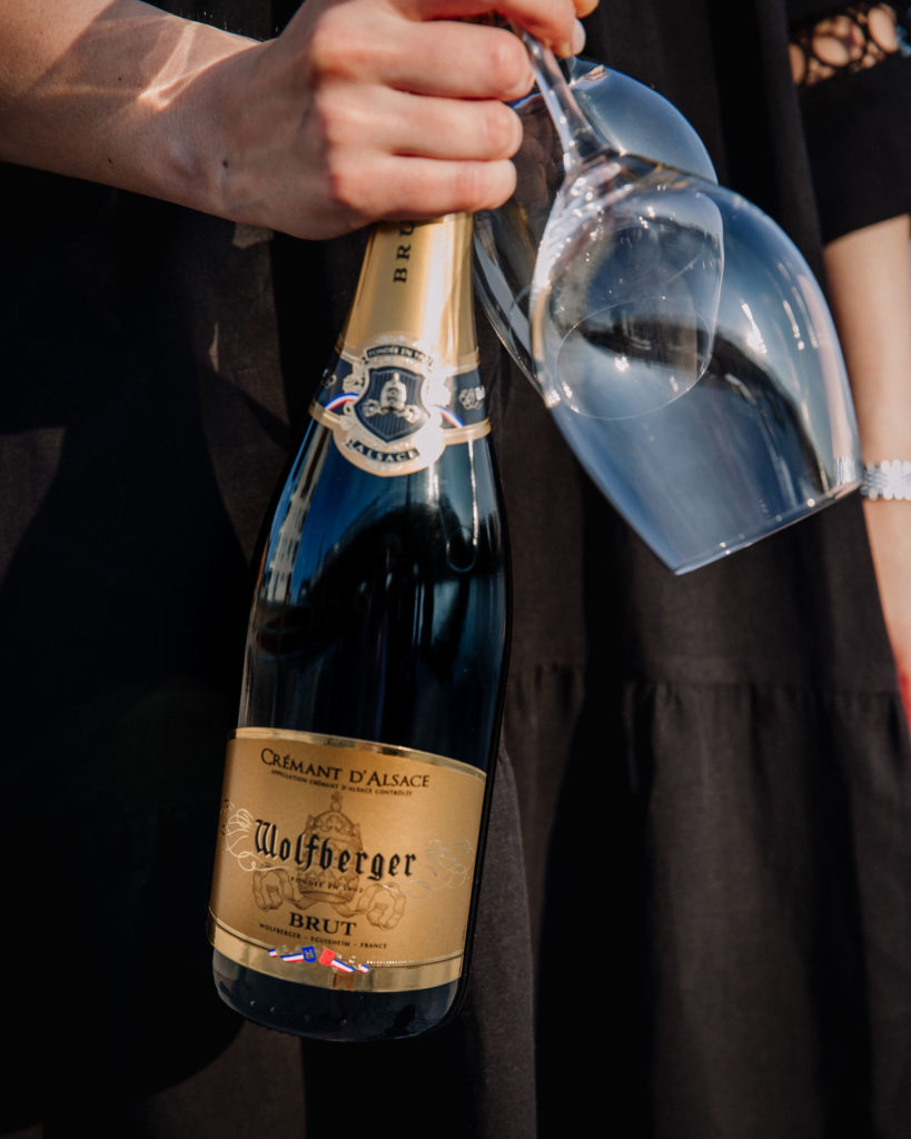 Wolfberger Crémant d'Alsace brut -viini on Kokkipottilan kuukauden viinisuositus. Kuvassa pullo on naisen kädessä. Kädessä on myös kaksi viinilasia.