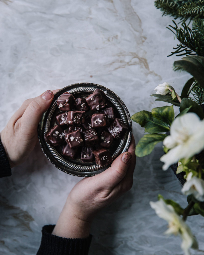 Maailman parhaat pipari-suklaakohvehdit on pyöreällä pienellä lautasella, jota kädet pitelevät. Oikeassa reunassa kuvaa on kukkia.