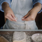 Rahkavoitaikina on taiteltu leivinlaudalle. Kuvassa käsistä ripotellaan jauhoja taikinan päälle.