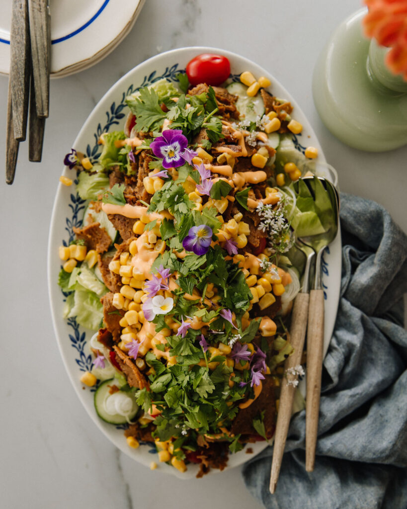 Ruokaisa salaatti seitanilla on moneen tilanteeseen sopiva ruoka. Salaatti on vegaaninen.
Kuvassa salaatti on soikealla vadilla. Päällimmäisenä on yrttejä ja syötäviä kukkia. Kuva ylälaidassa on lautaspino sekä haarukoita sekä osa kukkavaasista. Oikeassa alakulmassa on kankainen servetti. Kuva on otettu ylhäältäpäin.