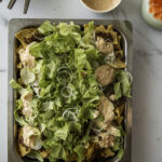 Big Mac -nachopelti hurmaa. Nachojen päällä on hampurilaisesta tuttuja makuja. Päällimmäisenä on rapeaa salaattia ja sipulirenkaita sekä kastiketta. Kuva ylälaidassa on lautasia ja haarukoita sekä kukkia.