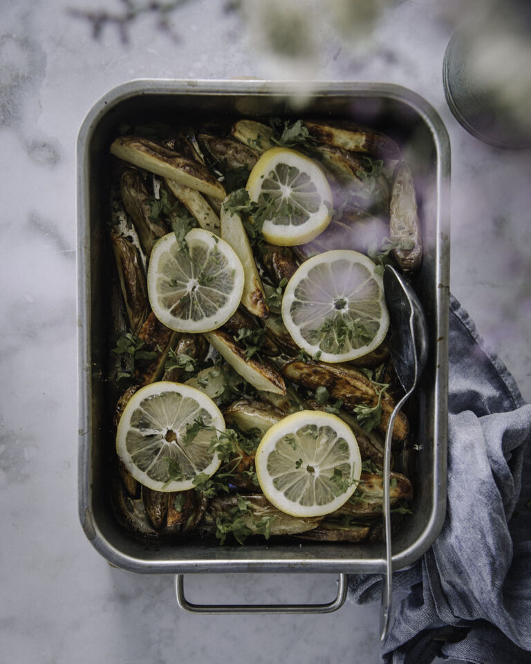 Sitruunaperunat on kreikkalaishenkinen lisäke, joka on helppo tehdä uunissa. Kuvassa sitruunaperunat ovat metallisessa uunivuoassa. Perunoiden päällä on sitruunaviipaleita ja silputtuja yrttejä.