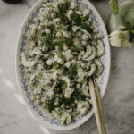 Tzatziki-kikhernesalaatti on helppo ja herkullinen lisäke. Kuvassa salaatti on vaalealla soikealla lautasella, jossa on sininen kuvio reunalla. Salaatin päällä on tilliä ja mintunlehtiä.