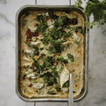 Helppo dumpling-paistos valmistuu alle puolessa tunnissa uunissa. Kuvassa ruoka on suorakulmaisessa uunivuoassa. Ruoan päällä on kesäsipulia, korianteria ja rapeaa valkosipuli-chiliöljyä. Kuvan oikeassa yläkulmassa on korianteripuska.