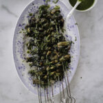 Sienivartaat on helppo grilliruoka. Kuvassa vartaat on metallisissa tuplatikuissa. Grillattujen vartaiden päällä on vihreää chimichurri-kastiketta ja yrttisilppua. Vartaat ovat soikealla vadilla.