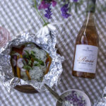 Kalanyytti grillissä on helppo kesäruoka. Kuvassa foliossa olevassa kalanyytissä on kalan ja perunoiden päällä kasviksia, yrttejä ja jogurttikastiketta. Nyytin vieressä on roseviinipullo.