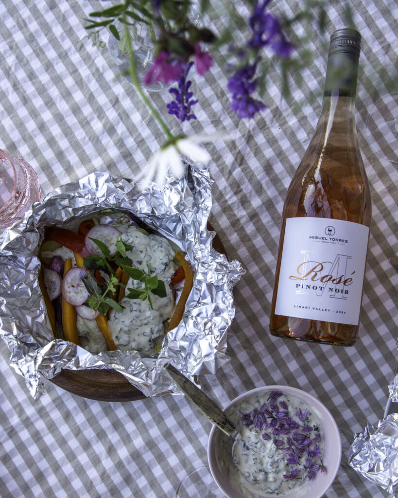 Kalanyytti grillissä on helppo kesäruoka. Kuvassa foliossa olevassa kalanyytissä on kalan ja perunoiden päällä kasviksia, yrttejä ja jogurttikastiketta. Nyytin vieressä on roseviinipullo.