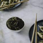 Hoisin-kastike on aasialainen kastike, joka sopii dipiksi, pöytämausteeksi tai vaikka wokkien viimeistelyyn. Kuvassa kastike on pienessä valkoisessa kulhossa. Kuvan oikeassa alalaidassa ja vasemmassa yläkulmassa on lautaset, joilla on dumpingeja.