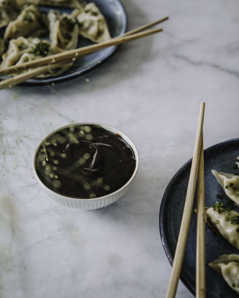 Hoisin-kastike on aasialainen kastike, joka sopii dipiksi, pöytämausteeksi tai vaikka wokkien viimeistelyyn. Kuvassa kastike on pienessä valkoisessa kulhossa. Kuvan oikeassa alalaidassa ja vasemmassa yläkulmassa on lautaset, joilla on dumpingeja.